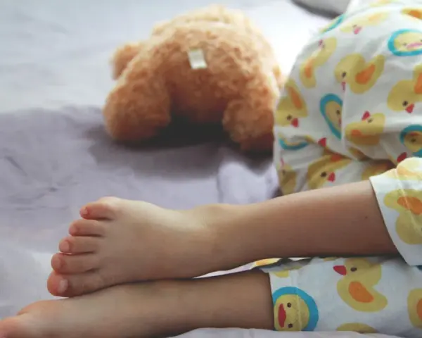 Ein Kind schläft im Pyjama mit Entenmuster, ein Teddybär liegt daneben. Es ist ein friedlicher Moment, in dem das Kind nachts ein und merkt es nicht.