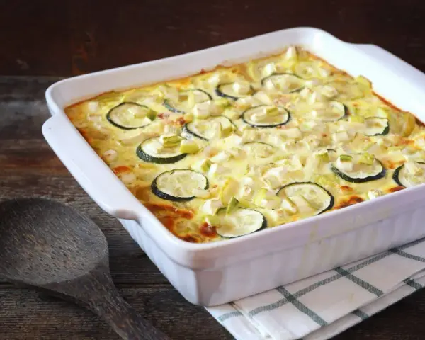 Un délicieux gratin de courgettes, prêt à être dégusté, avec des rondelles de courgettes et des morceaux de poireau dans une sauce crémeuse.