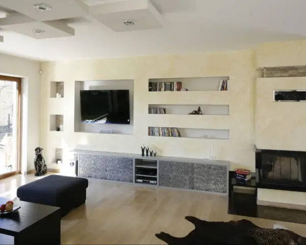 Nowoczesna zabudowa pod telewizor z karton gipsu, z wnękami na książki i dekoracje.