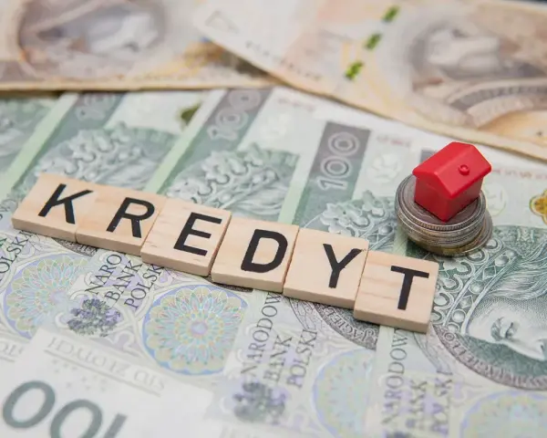 Litery układające słowo "KREDYT" na banknotach. Mały czerwony domek na stosie monet symbolizuje pomoc w spłacie kredytu, np. z funduszu wsparcia kredytobiorców.