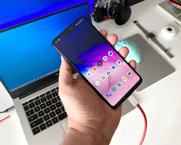 Smartfon podłączony do laptopa, gotowy do przesyłania zdjęć za pomocą aplikacji.