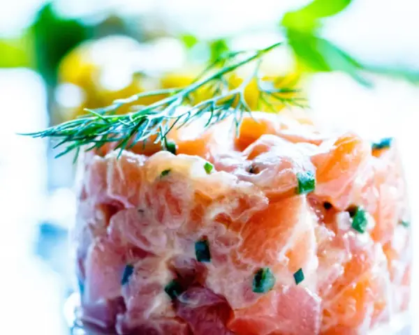 Tartare di salmone fresco, finemente tagliato e condito, guarnito con aneto. Un piatto leggero e saporito.
