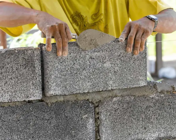 Murarz układa bloczek betonowy, sprawdzając jego wymiary.