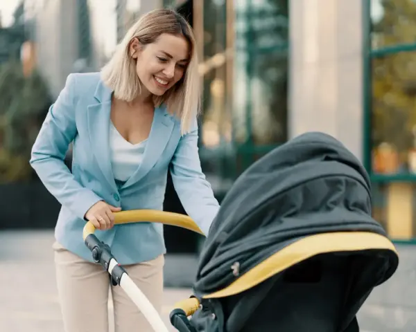 Uśmiechnięta kobieta w eleganckim stroju, z wózkiem dziecięcym, symbolizuje powrót do pracy po macierzyńskim.