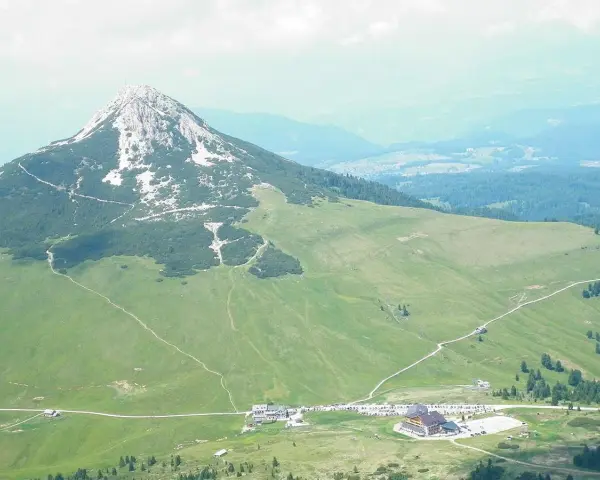 Panoramica delle malghe al Passo Lavazè, con un imponente monte sullo sfondo e sentieri che si snodano tra prati verdi.