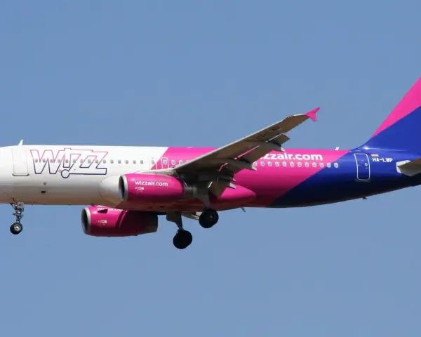Samolot Wizz Air z różowo-fioletowym ogonem leci na tle błękitnego nieba. Sprawdź wizz discount club cena i leć taniej!
