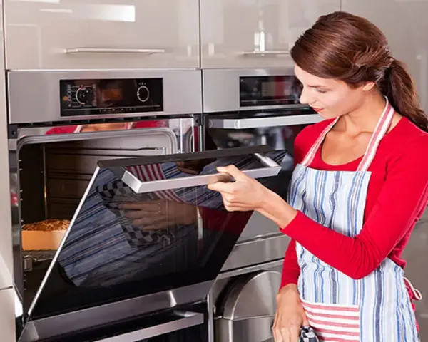 Mujer con delantal abre horno donde se hornea un pan.