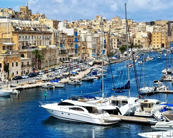 Malta plan zwiedzania: malowniczy port z łodziami i zabytkowymi budynkami w tle.