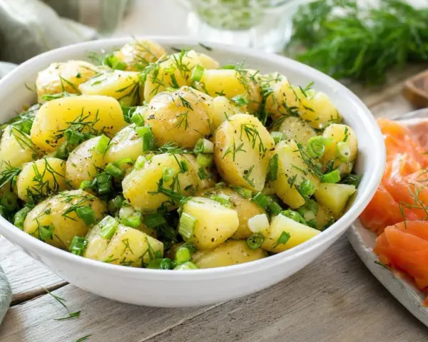 Salade de pommes de terre fraîchement préparée, garnie d'aneth et de ciboule, prête à être servie avec une sauce légère.