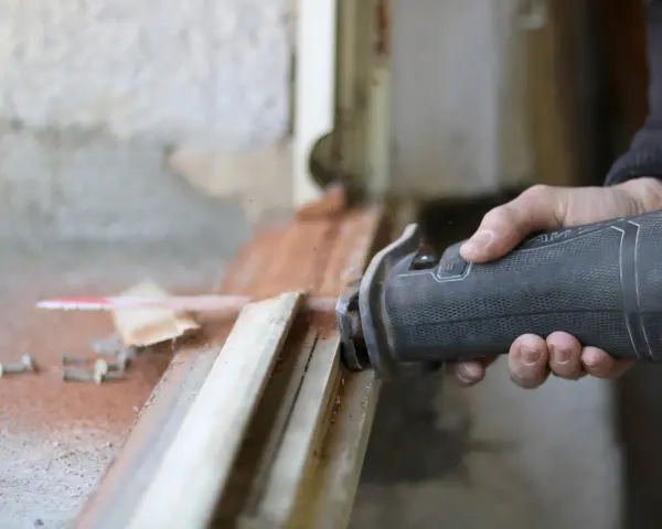 Main d'un artisan utilisant une scie sauteuse pour la dépose totale d'une fenêtre. Estimation du prix pose fenêtre dépose totale.