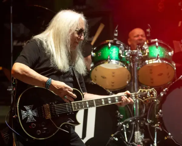 Uriah Heep członkowie na scenie. Mick Box gra na gitarze, a za nim perkusista.