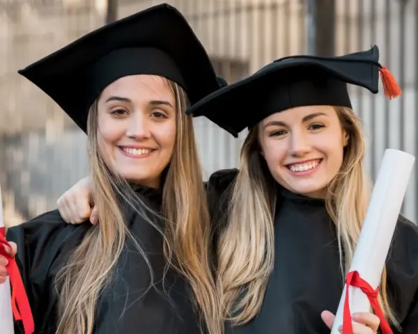 Dwie uśmiechnięte absolwentki medycyny w togach i biretach trzymają dyplomy. Gratulacje z okazji ukończenia studiów medycznych!
