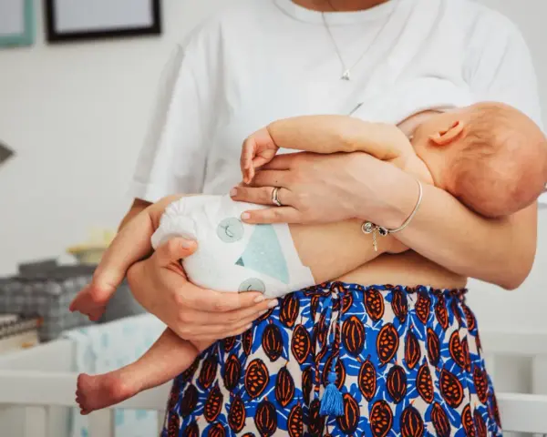 Mama tuli noworodka w pieluszce, idealnie jak ubierać noworodka latem. Lekkie ubranko i pieluszka to klucz do komfortu.