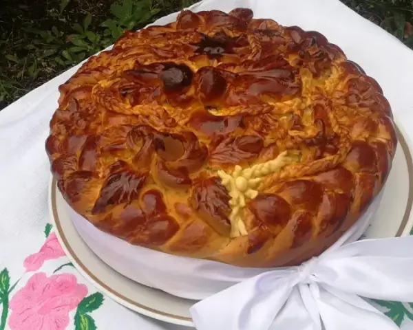 Obrzędowe ciasto weselne, bogato zdobione, z plecionkami i kwiatami z ciasta, na haftowanym obrusie.