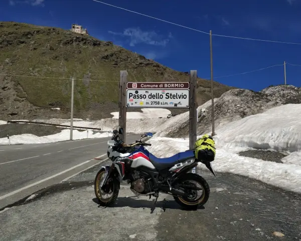 Moto pronta per affrontare il Passo dello Stelvio, con neve ai lati della strada e un edificio in cima alla montagna.