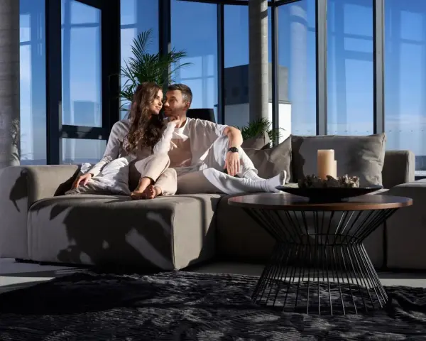 Pareja disfrutando de un momento íntimo en un sofá moderno, ideal para alquileres de temporada con vistas panorámicas.