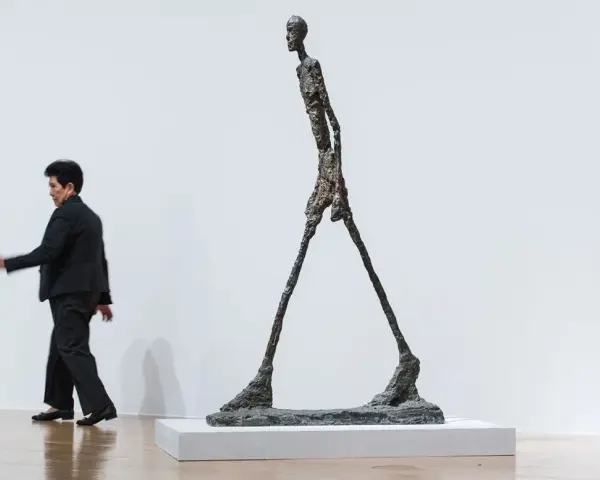 Un homme qui marche, une sculpture élancée, semble se déplacer dans un espace blanc.
