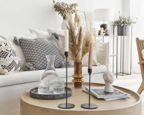 Tavolino rotondo in legno con elementi decorativi che evocano un'atmosfera boho chic: vasi, candele, libri e una scultura di testa.