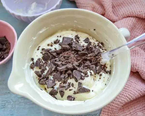 Cremige Masse mit Schokoladenstückchen, bereit für das Herrencreme Rezept. Kleine Schale mit gehackter Schokolade daneben.