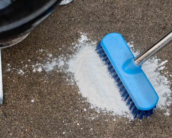 A blue brush is used to scrub a pile of white powder on a concrete patio, demonstrating how to clean concrete patio.