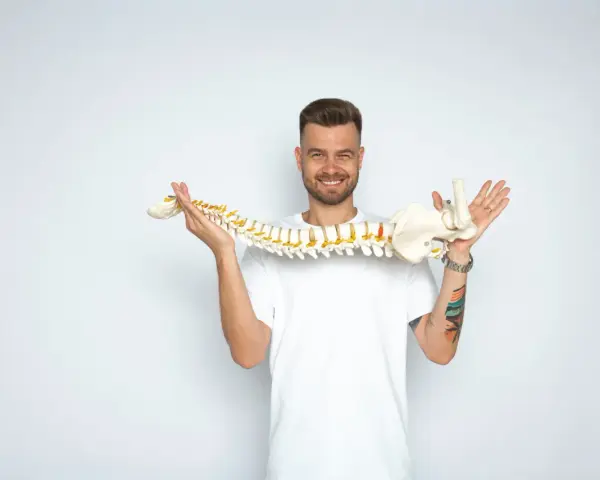 Uśmiechnięty mężczyzna trzyma model kręgosłupa, jakby prezentował jego elastyczność, niczym worek oponowy.