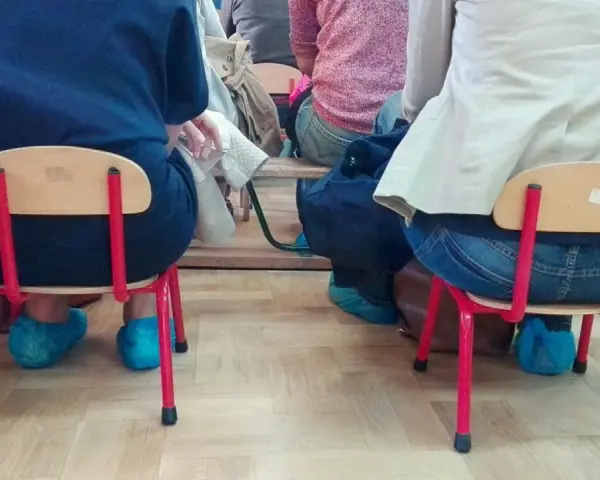 Dostateczny, jaka to ocena? Dzieci siedzą na małych krzesełkach w niebieskich ochraniaczach na buty.
