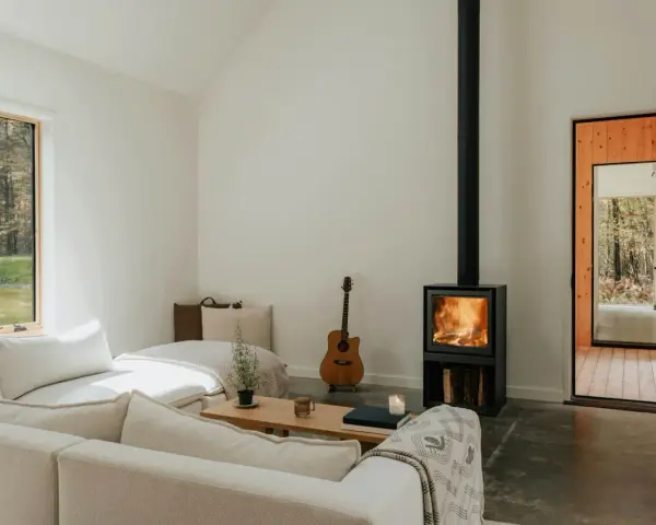 Salon cosy avec poêle à bois allumé, guitare et canapé. Une aide financière pour le tubage de cheminée pourrait rendre ce lieu encore plus chaleureux.
