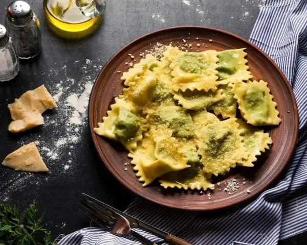 Pyszne ravioli z zielonym farszem, posypane parmezanem. Obok kawałki sera i przyprawy, gotowe do podania.
