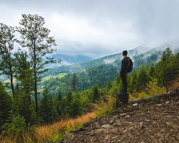 Mężczyzna z plecakiem podziwia mglisty górski krajobraz. To właśnie jest trekking – odkrywanie natury pieszo.