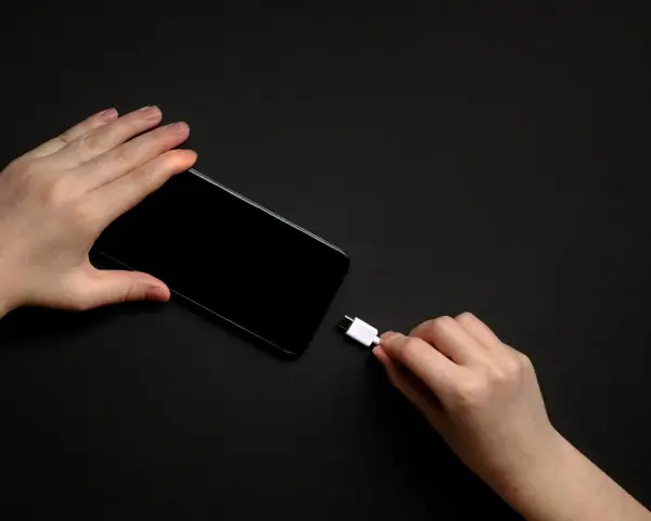 Dwie dłonie trzymają smartfon i biały kabel USB-C. Zastanawiasz się, do ilu procent ładować telefon, by zadbać o jego baterię?
