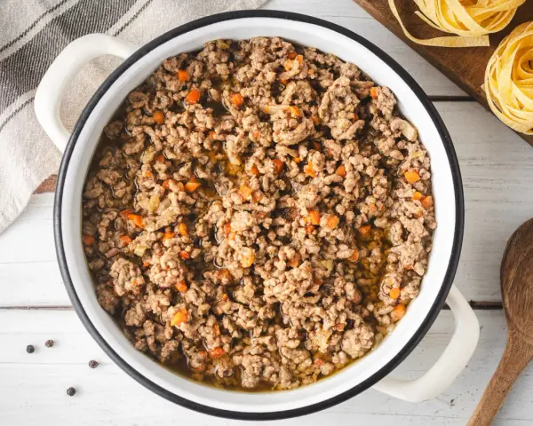 Un saporito ragù bianco in una pentola, pronto per condire la pasta. Pezzetti di carota e cipolla si mescolano alla carne macinata.