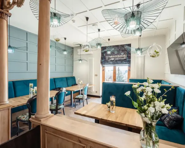 Wnętrze restauracji z turkusowymi kanapami, drewnianymi stołami i ozdobnymi lampami.
