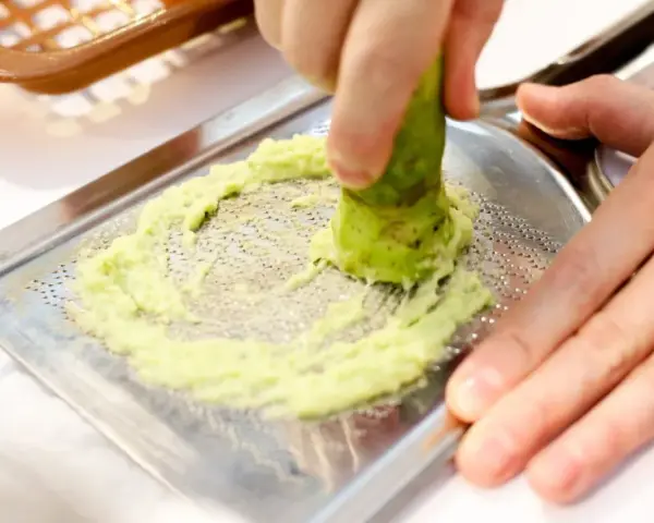 Świeże wasabi jest tarte na metalowej tarce, tworząc zieloną pastę. To właśnie tak powstaje prawdziwe wasabi.