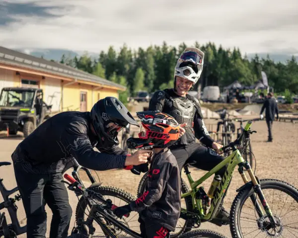 Två cyklister förbereder sig för mtb downhill. En vuxen hjälper ett barn med hjälmen.