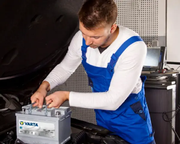Mechanik w niebieskim kombinezonie wykonuje kodowanie akumulatora Varta w samochodzie.