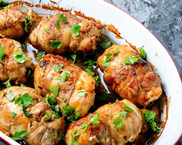 Involtini di carne dorati e succulenti, guarniti con prezzemolo fresco, cotti in una teglia bianca.