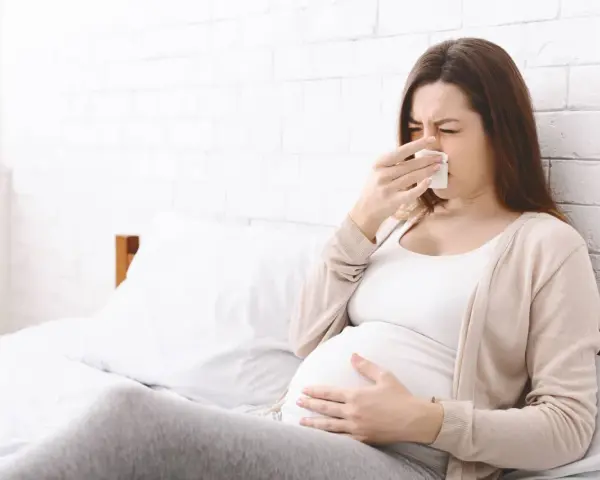 Kobieta w ciąży z chusteczką przy nosie, czuje się niedobrze.