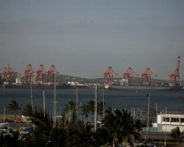 Port w Durban, RPA, z czerwonymi dźwigami portowymi i statkami towarowymi na tle wzgórz. Na pierwszym planie widać maszty jachtów.