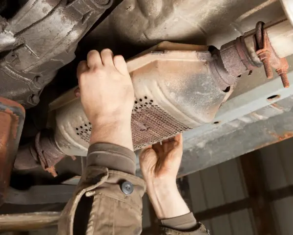 Mechanic inspecting a catalytic converter, a common culprit for why does my car smell like rotten eggs.