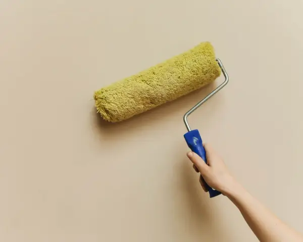 En hand håller en färgroller med gul päls, redo att måla en vägg. Kanske är det dags för en 3m rubbing för att fräscha upp hemmet.