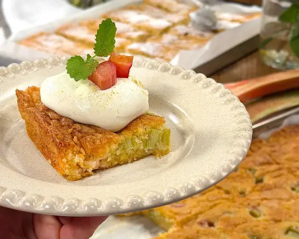 En bit saftig rabarberkaka i långpanna, toppad med fluffig grädde och mynta. Perfekt för fikat!