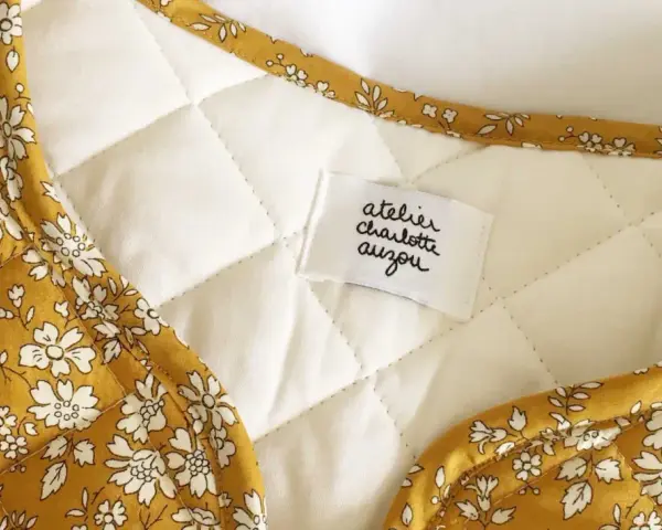 Détail d'une veste matelassée femme avec un tissu fleuri jaune moutarde. Un patron gratuit pour créer ce modèle est disponible.