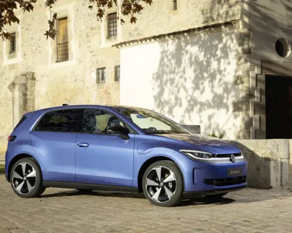 Niebieski samochód elektryczny VW ID. Polo stoi na brukowanej drodze przed kamiennym budynkiem.