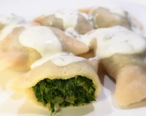 Pierogi ze szpinakiem polane sosem śmietanowym na białym talerzu.