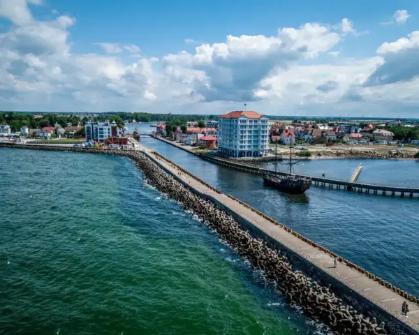 Widok na port w Darłówku z falochronem, statkiem pirackim i nowoczesnym budynkiem.