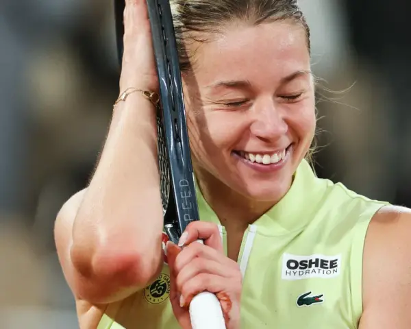 Szczęśliwa Iga Świątek, zwyciężczyni Roland Garros, z rakietą opartą o głowę, w geście triumfu.