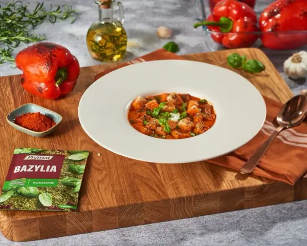 Aksamitny krem z pieczonej papryki z grzankami i bazylią. Obok składniki: papryka, oliwa, czosnek, przyprawy.