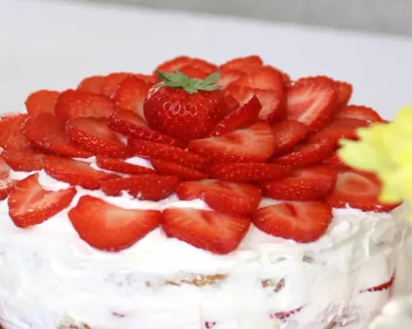 En vacker vegansk jordgubbstårta täckt med färska jordgubbar och fluffig grädde. Perfekt för sommaren!