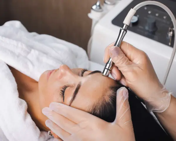 Aesthetician performs microdermabrasion on a woman's forehead. The question of microdermabrasion how often depends on skin type and goals.