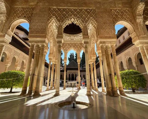 Intricate arches and columns of the Alhambra, a perfect postcard from Granada. Sunlight streams through, illuminating the detailed stonework.